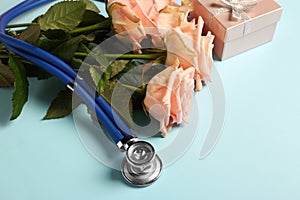 Stethoscope, gift box and flowers on light blue background, closeup with space for text. Happy Doctor\'s Day