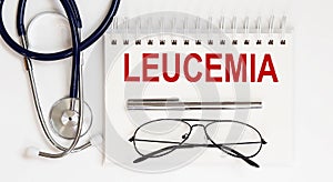 Stethoscope,glasses and pen with notepad with text LEUCEMIA photo