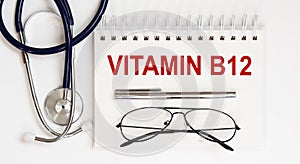 Stethoscope,glasses and pen with notepad with text VITAMIN B12 on white background