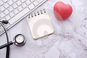 Stethoscope, heart, keyboard and notepad on tile background