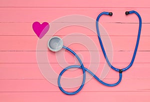 Stethoscope and heart on pastel pink wooden table. Cardiology equipment for diagnosing cardiovascular diseases. Top view.