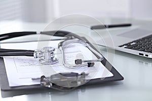 Stethoscope lying at the desk with medical history records and laptop computer. Medicine doctor`s working table concept
