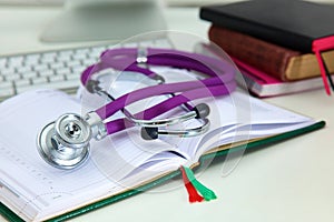 Stethoscope lying on a notebook computer in the background and books