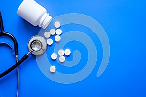 Stethoscope and meds on doctors workplace on blue background top