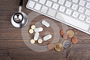 Stethoscope, money and pills at the computer keyboard on a wooden table