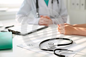 Stethoscope next to hand of doctor reassuring her female patient. Medical ethics and trust concept