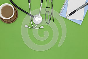 Stethoscope with notebook ,pen, white paper ,coffee cup,glasses, on green background,Medical background concept.