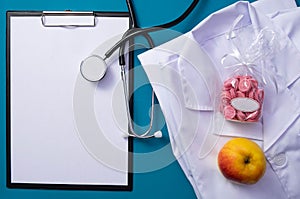 Stethoscope, notepad, heart, apple, vitamins, pills, folded form of a doctor lie on the table