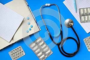 Stethoscope, notepads and medicines on a blue background, top view