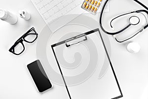 Stethoscope in the office of doctors.Top view of doctor`s desk table, blank paper on clipboard with pen. Copy space