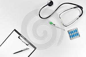 Stethoscope in the office of doctors.Top view of doctor`s desk table, blank paper on clipboard with pen. Copy space