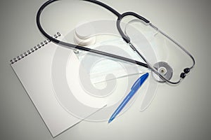 Stethoscope in the office of doctors.Top view of doctor`s desk table, blank paper on clipboard with pen. Copy space