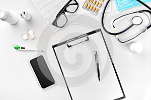 Stethoscope in the office of doctors.Top view of doctor`s desk table, blank paper on clipboard with pen. Copy space