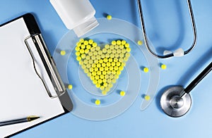 Stethoscope and a pad with pen and pills on a blue wooden background