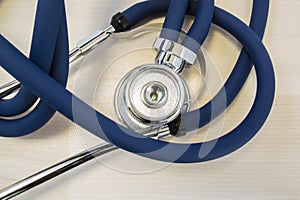 Stethoscope or phonendoscope for heart or lung auscultation with blue two air tubes lies on a light wooden desk in the doctor`s of photo