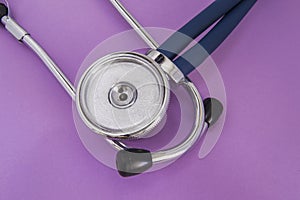 Stethoscope or phonendoscope lying on a purple background big head diaphragm, plastic disc upwards near the earpieces closeup