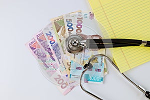 Stethoscope phonendoscope on a Ukrainian money grivna with banknotes on yellow notebook write in the white background