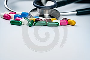 Stethoscope with pile of antibiotic capsule pills on white background. Antimicrobial drug resistance and overuse. Medical