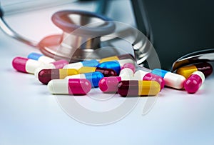 Stethoscope with pile of colorful antibiotic capsule pills on white table with drug tray. Antimicrobial drug resistance