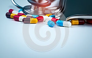 Stethoscope with pile of colorful antibiotic capsule pills on white table with drug tray. Antimicrobial drug resistance