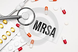Stethoscope, pills and notebook with mrsa word on medical desk