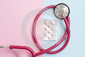 A stethoscope and pills. Plate with tablets on a pink blue background.