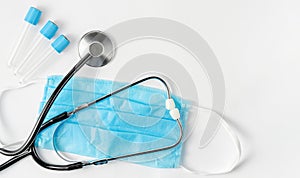 Stethoscope on protective mask and empty container for blood test on white background. Medical examinations.