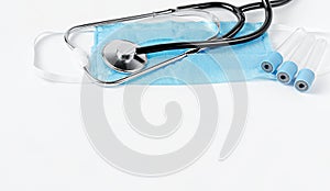 Stethoscope on protective mask and empty container for blood test on white background. Medical examinations.