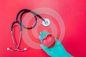 Stethoscope and red heart in hand in rubber glove on red background