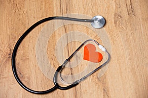 Stethoscope with red heart shape inside, on wooden background. Health and medicine symbol. Heartbeat for flyers, poster, web,