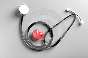 Stethoscope and small red heart on gray background.