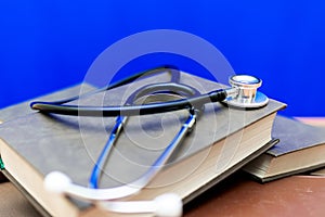 Stethoscope with stack of books on table or blue background.Medical literature concept