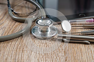 Stethoscope with syringe, pen, tablet and dental tools on wooden table