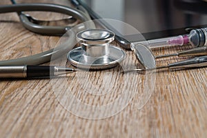 Stethoscope with syringe, pen, tablet and dental tools on wooden table