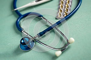 A stethoscope on a textured background, pills, thermometer blur