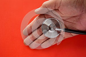 Stethoscope on top of a doctor hand with red background.