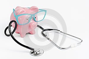 Stethoscopeand piggy bankwith glasses on white background. Medical insurance coverage