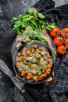 Stew with chicken hearts and vegetables with fresh parsley. Black background. Top view