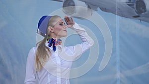 Stewardess salutes in aeroport and smiles looking at camera on blue background