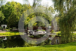 Stewart Park, a view of the red footbridge and old stone house surrounded by trees, view from pond in summer. Perth