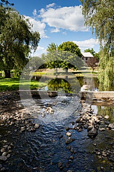 Stewart Park, a view of tree with rocky stream in the foreground, multiple stones, reflected on pond in summer. Perth