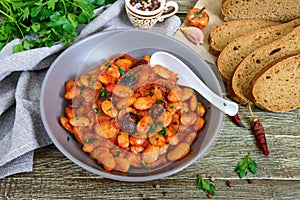 Stewed broad beans in tomato sauce with herbs and spices close-up, slices of rye bread