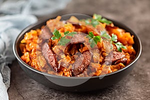 Stewed cabbage with sausages in black plate. horizontal view from