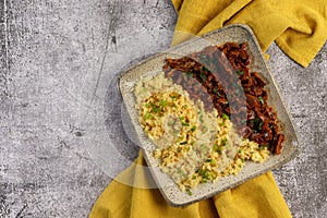 Stewed chicken gizzards with boiled rice on a square plate on a dark gray background