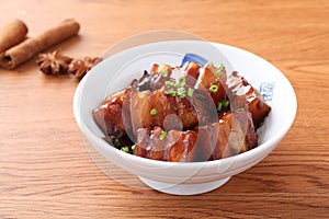 Stewed meat of pork in chinese style in white bowl in wooden tab