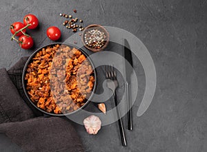 Stewed oxtails with vegetables in a black plate on a dark background with fresh tomatoes. Meat stew. The concept of traditional