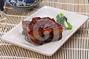 Stewed pork meat in chinese style on white plate on bamboo tray