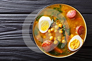 Stewed Potaje de garbanzos chickpeas, spinach, chorizo sausages, boiled eggs close-up in a bowl. horizontal top view