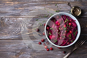 Stewed red cabbage with apples, cranberries, spices and greens on a wooden background