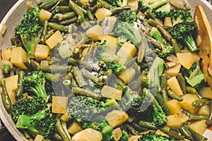 Stewed vegetables in frying pan: broccoli, green beans, potatoes, onions and spices. vegetarian food, top view